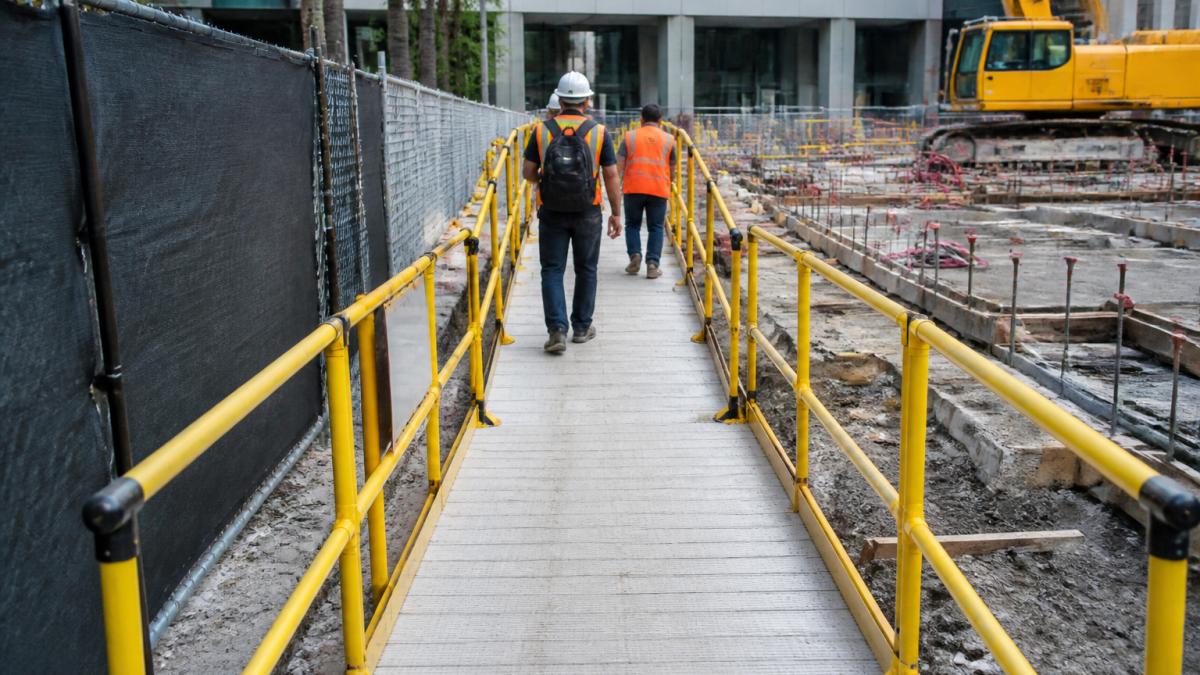 Construction site with clearly marked accessible pedestrian detour featuring temporary ramps, directional signage, yellow safety barriers, and firm walkway surfaces guiding workers and visitors around the active work zone in daylight