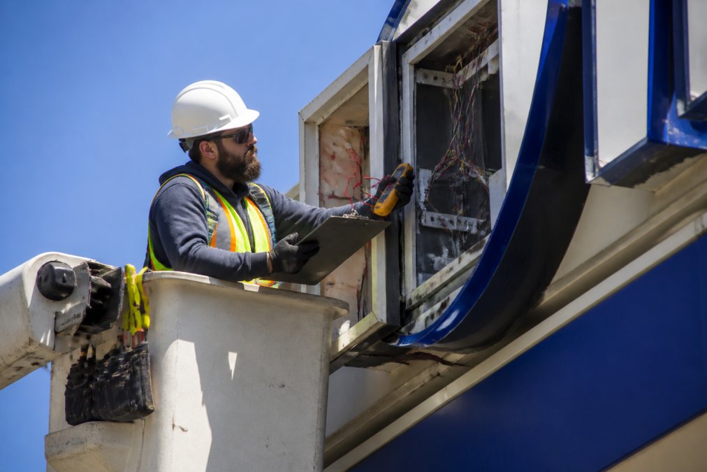 Technician in a bucket truck performing sign repair on electrical wiring