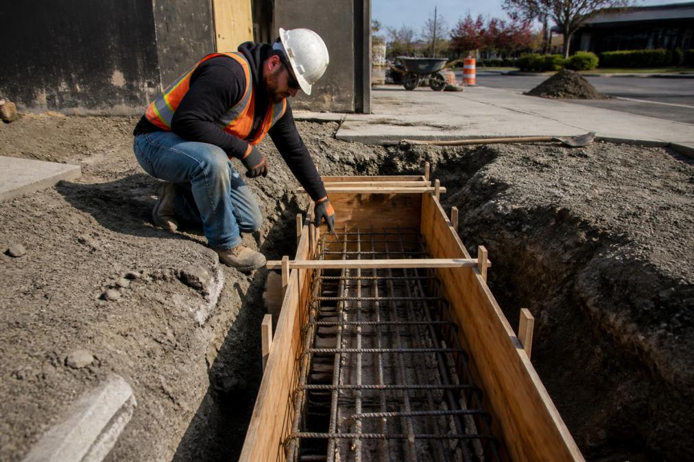 Construction worker inspecting a concrete footer with rebar during a monument sign installation process.